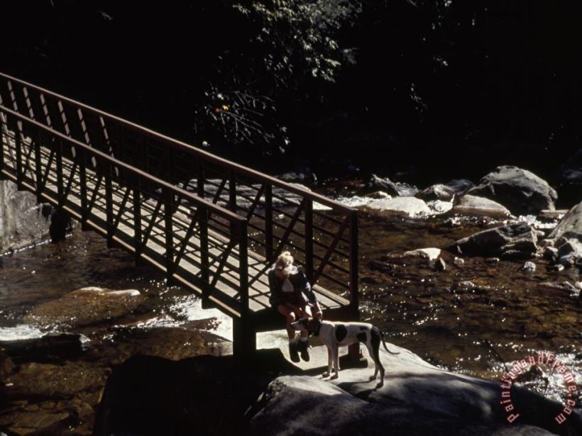 Woman And Dog Resting at a Footbridge Across The Whitewater River painting - Raymond Gehman Woman And Dog Resting at a Footbridge Across The Whitewater River Art Print